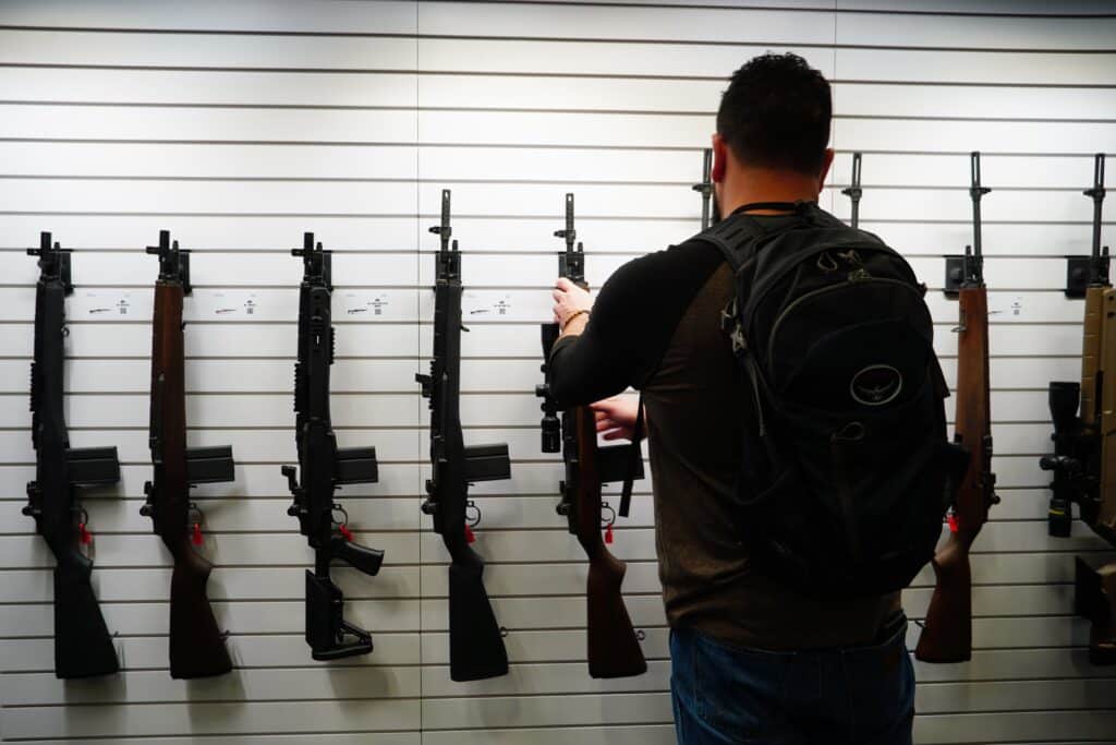 An attendee at the 2024 NRA Annual Meeting examines a row of rifles